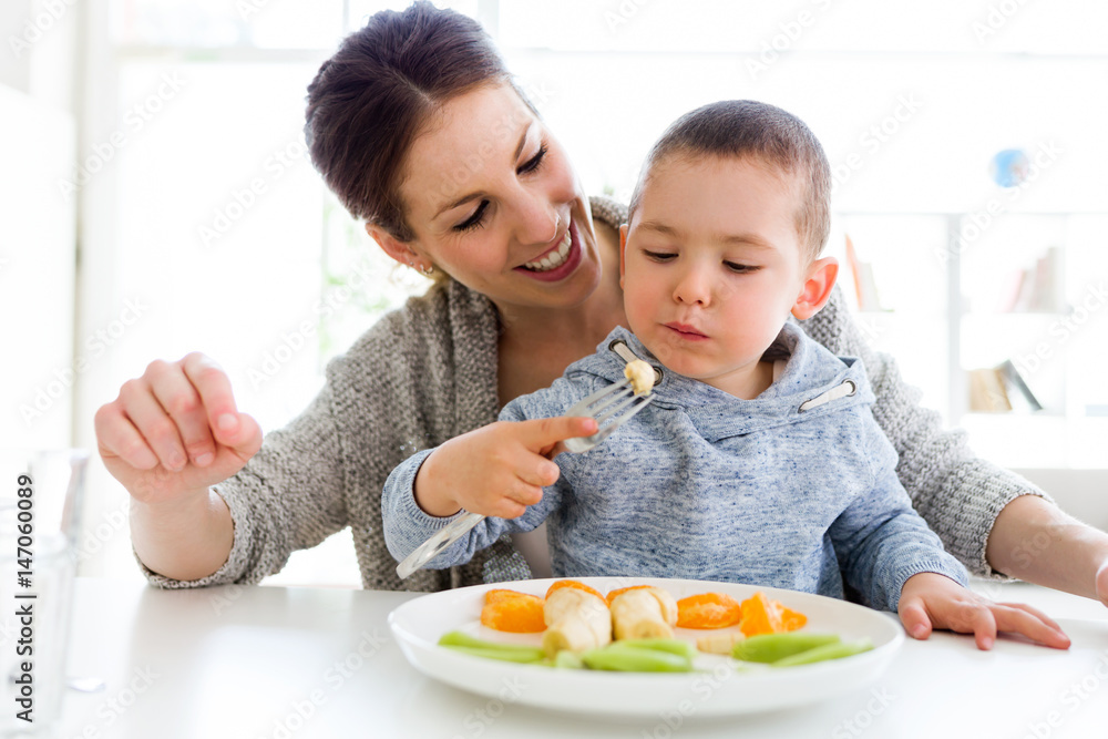 Beautiful young mother and her son eating fruits at home.
