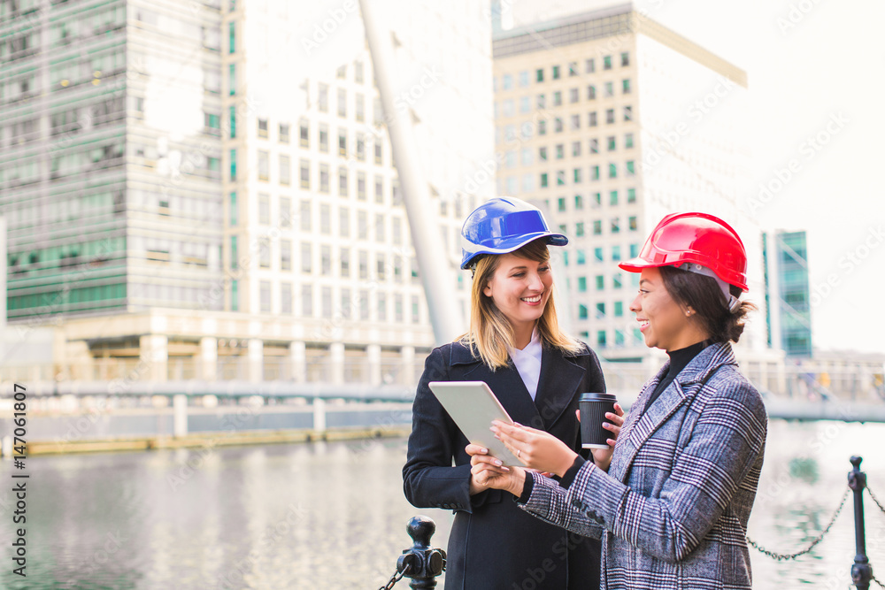 Two successful engineers stand together with the tablet and cup of coffee in hands and discuss a new project outdoor Two successful engineers stand together with the tablet and cup of coffee in hands and discuss a new project outdoor