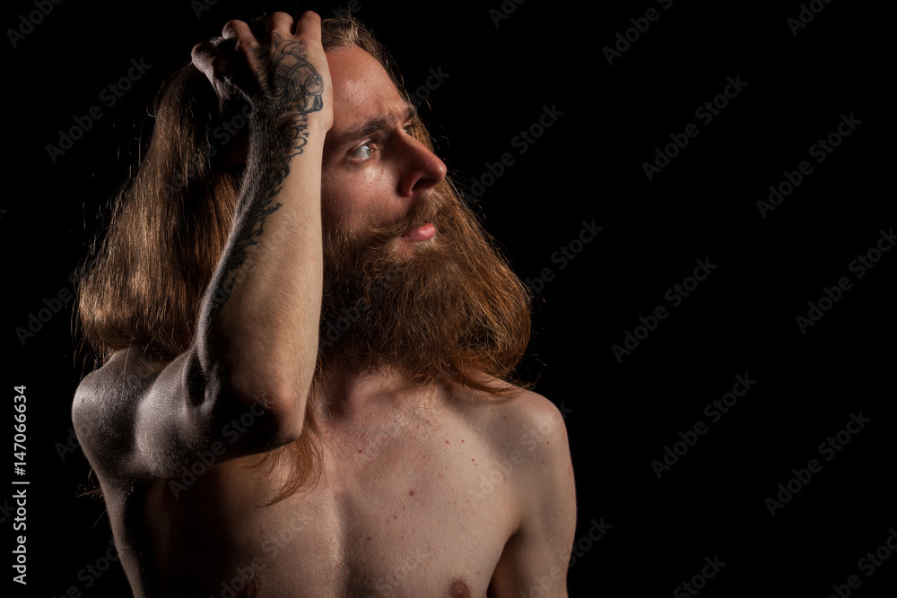 Cool looking tattooed bearded hipster on black background in studio photo. Expression and fashion