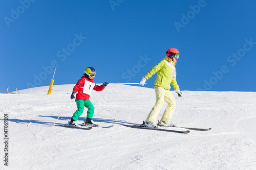 Sporty mother pulling her kid son on ski by a pole