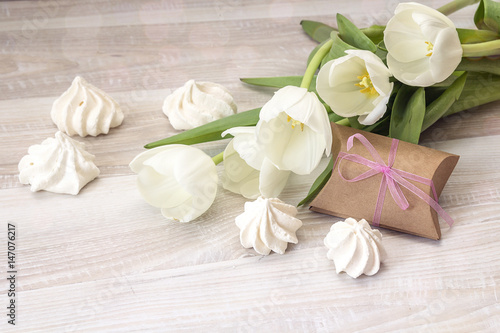 Background with white tulips, gift box and meringue cookies on wooden table. Mother's Day background.