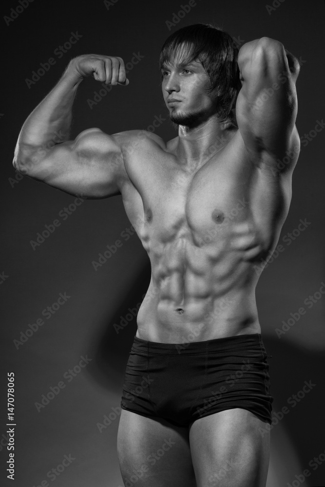 Portrait of strong healthy handsome Athletic Man Fitness Model posing near dark gray wall