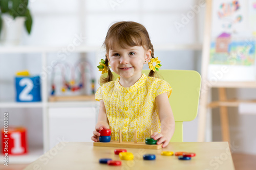 Kid girl playing with logical toy on desk in nursery room or kindergarten. Child arranging and sorting colors and sizes