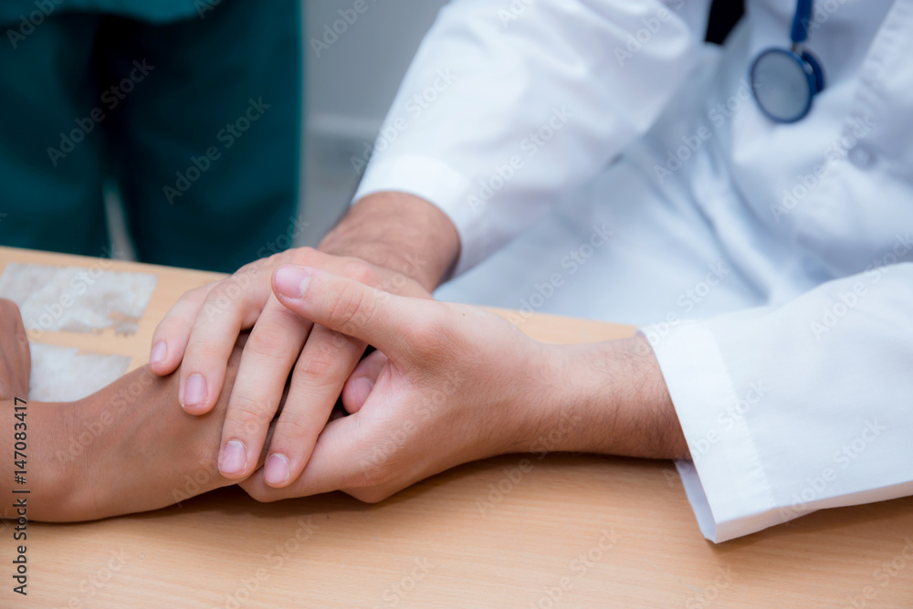 Friendly male doctor hand holding patient hand sitting at the desk for encouragement - empathy - cheering and support while medical examination. Friendly male doctor hand holding patient hand sitting at the desk for encouragement - empathy - cheering and support while medical examination.