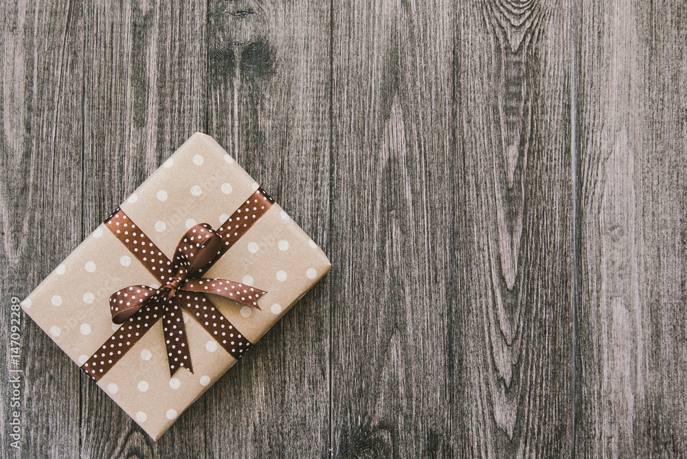 Box in craft paper, eco paper on the wooden table. Top view. Brown paper wrapped gift box with satin ribbon bow on a old rustic wood background. Background for your design. Retro filter Box in craft paper, eco paper on the wooden table. Top view. Brown paper wrapped gift box with satin ribbon bow on a old rustic wood background. Background for your design. Retro filter