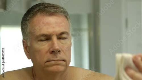 man looking in the bathroom mirror at the rosacea on his face