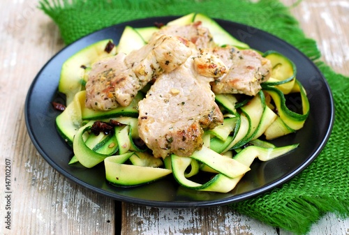 Vegetable zucchini noodles with spicy pork fillet on black plate on wooden background