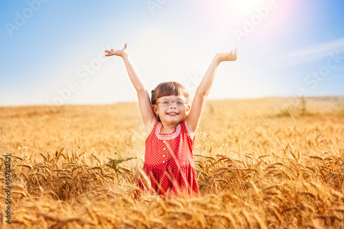 Little girl with arms outstretched in a wheat field, lens flare