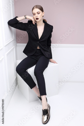 High fashion portrait of young elegant woman in black suit and loafers.