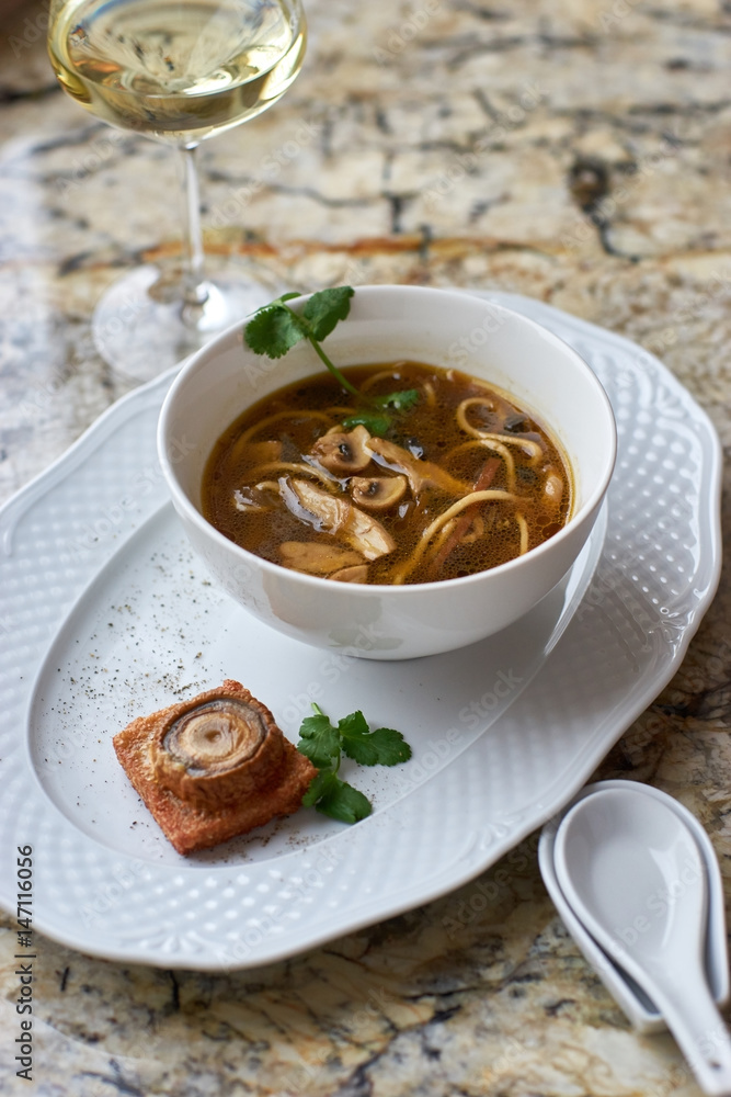 Asian cuisine. Mushroom soup with egg noodles served with toast, bread and white wine on marble background. Asian cuisine. Mushroom soup with egg noodles served with toast, bread and white wine on marble background.
