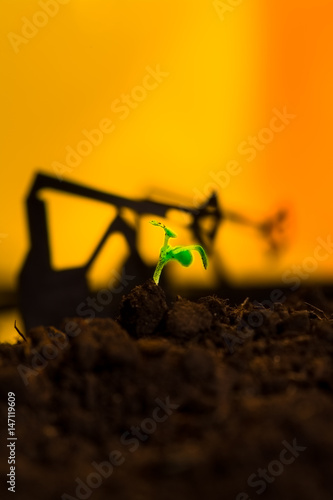 Young green plant in soil on background oil rocking machine photo