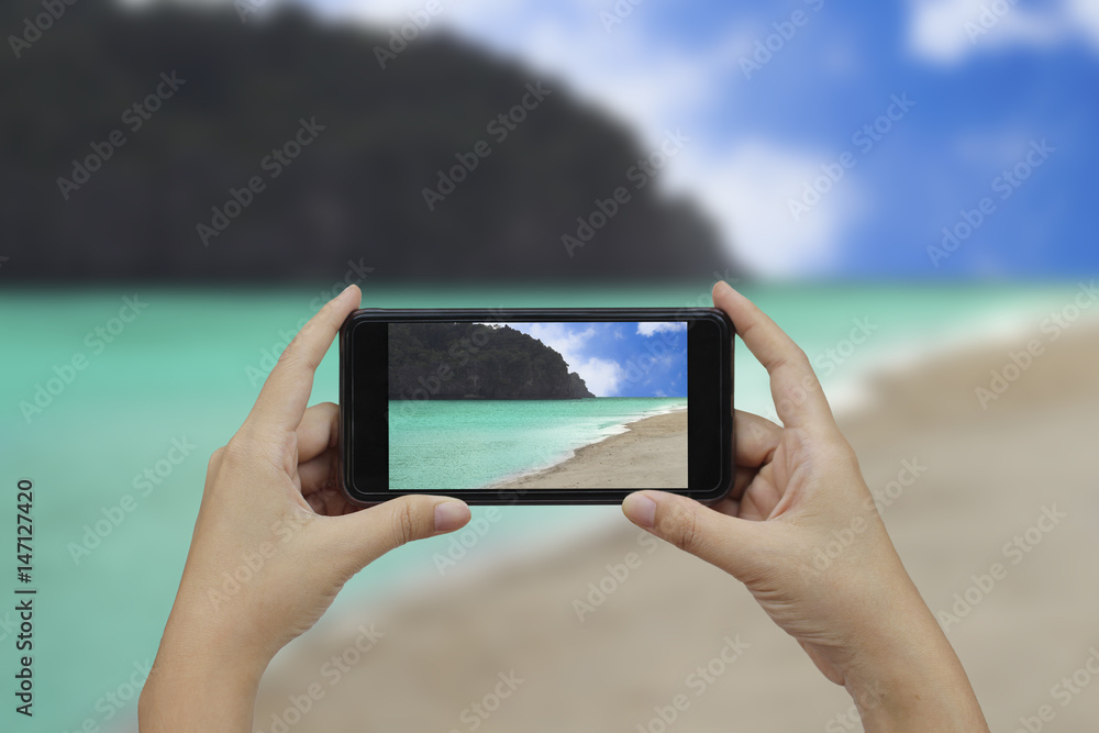 Hand holding smartphone with white blank screen over blurred beachside mountains background