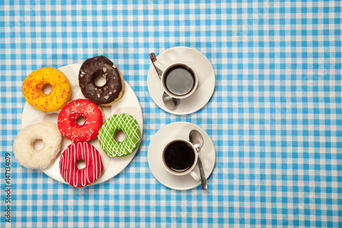 Two cups with coffee and donuts on a blue table