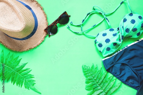 Flat lay of bikini and accessories with fern leaves on green background, Summer concept