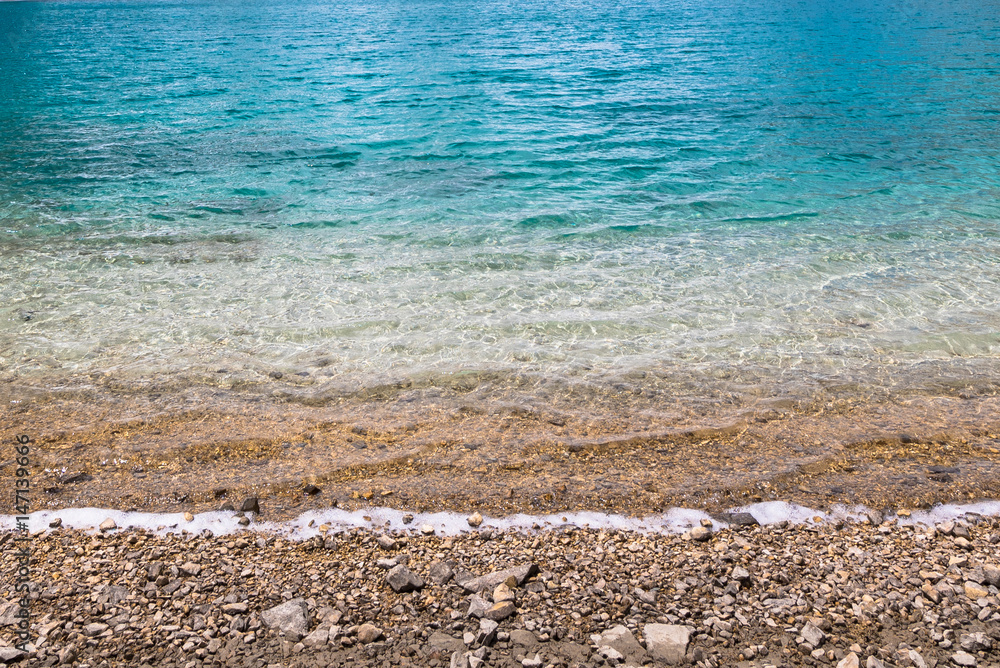 Obraz premium green blue water sea ocean background texture with pebbles.