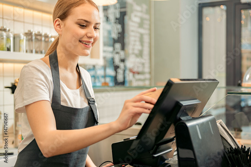 Cheerful shop assistant using digital device for payment