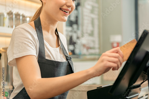 Cute female cashier holding credit card near monitor