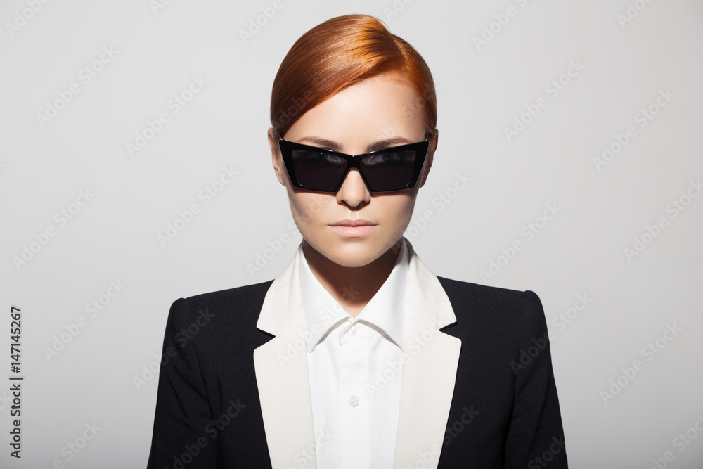 Fashion portrait of serious woman dressed as a secret agent or spy. Gray background.