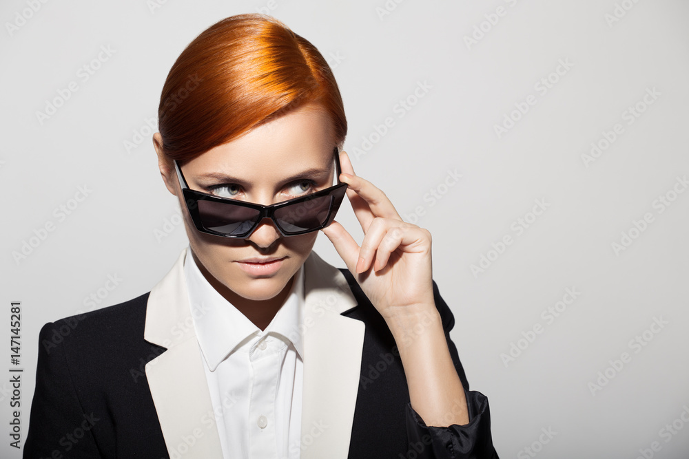 Fashion portrait of serious woman dressed as a secret agent or spy. Gray background.