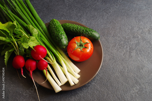 Fresh vegetables on a plate on a dark surface of a table. Healthy, vegetarian, organic food