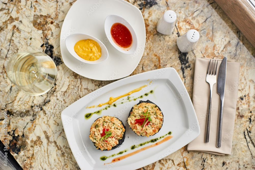 Crab cutlets with mashed potatoes with cuttlefish ink and spicy sauce served on white plate with glass of white wine on marble table Crab cutlets with mashed potatoes with cuttlefish ink and spicy sauce served on white plate with glass of white wine on marble table