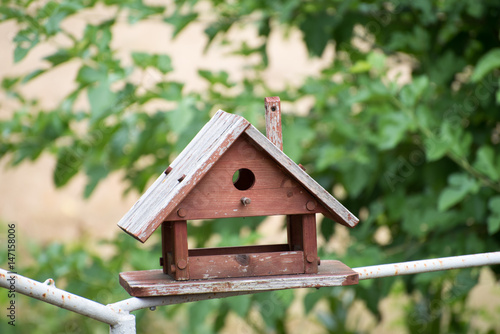 Brown wooden birdhouse with foliage blurred in background