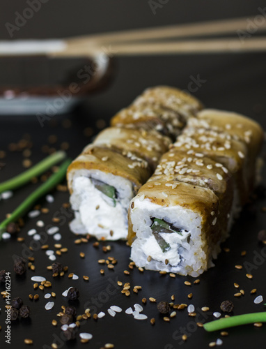 Eel sushi rolls with soy sauce and chopstics on black background 