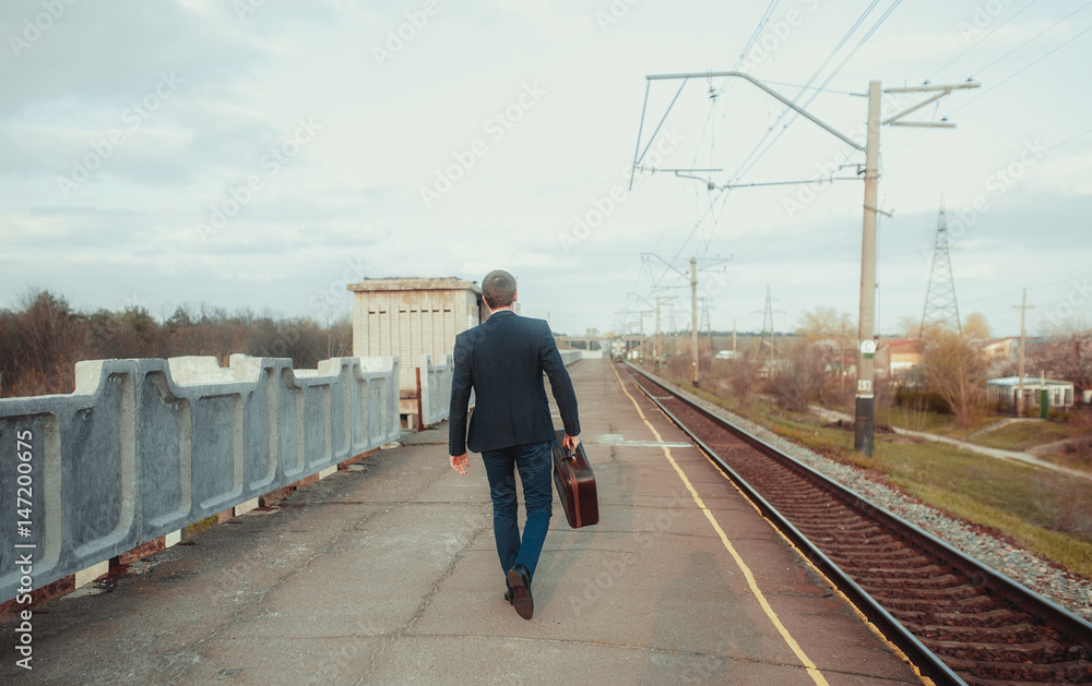 Businessman in suit with suitcase walks along the platform station. Business trip.