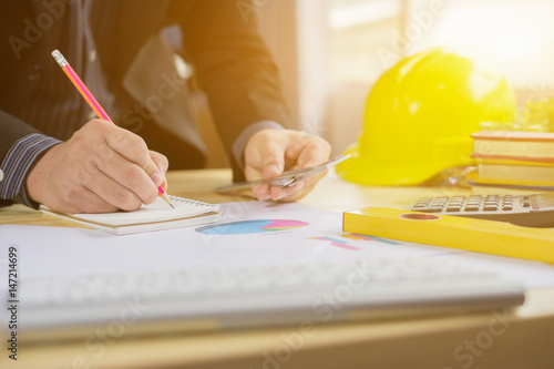 Architects working on blueprint with pencil,engineer inspective in workplace ,architectural project, blue prints,ruler,calculator,laptop and yellow helmet. Construction concept. Engineering tools photo