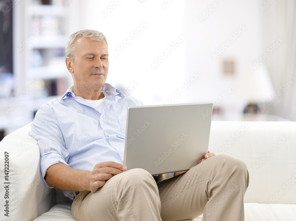 Browsing on the internet. Shot of a senior man using his laptop while relaxing at home. Browsing on the internet. Shot of a senior man using his laptop while relaxing at home.