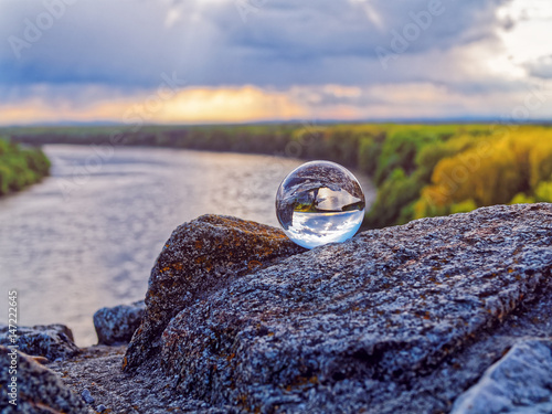 Magic glass ball on old stones. In the background is the bend of the river, spring forest and cloudy sky