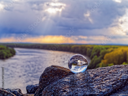 Magic glass ball on old stones. In the background is the bend of the river, spring forest and cloudy sky
