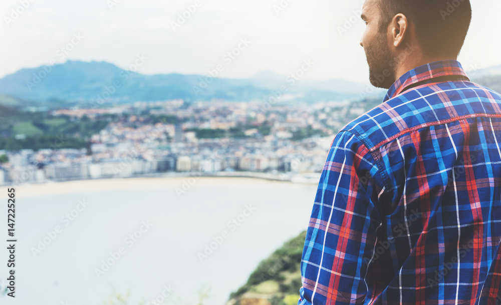 Hipster young man looking on observation deck in trip holiday in Bilbao, enjoying view on seascape on mountain and ocean, tourist traveler on background panoramic view of the city. Mock up for text Hipster young man looking on observation deck in trip holiday in Bilbao, enjoying view on seascape on mountain and ocean, tourist traveler on background panoramic view of the city. Mock up for text