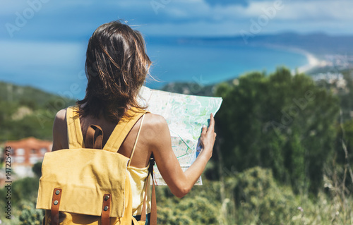 Hipster tourist hold and look map on trip, lifestyle concept adventure, traveler with backpack on background mountain and blue sea landscape horizon, young girl hiker pointing hands on trekking plan