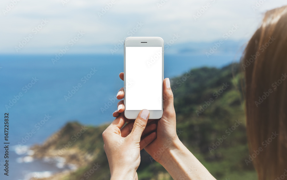 Hipster photograph on smart phone gadget mobile, mock up of blank screen. Traveler hold and using in female hand mobile on background mountain seascape horizon. Tourist look on blue ocean, lifestyle
