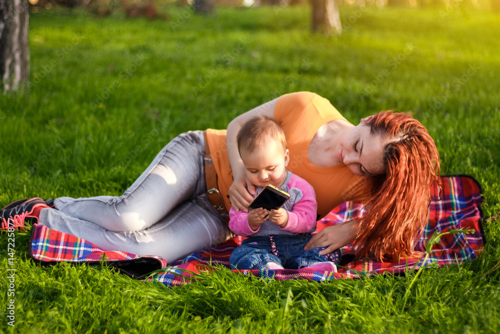 young beautiful woman playing with her baby on the plaid on green meadow young beautiful woman playing with her baby on the plaid on green meadow