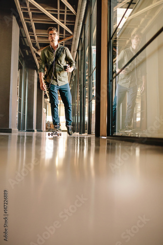 Casual businessman skating through office corridor