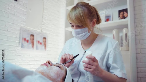 Cosmetician applying facial mask to the face of young woman in beauty salon photo