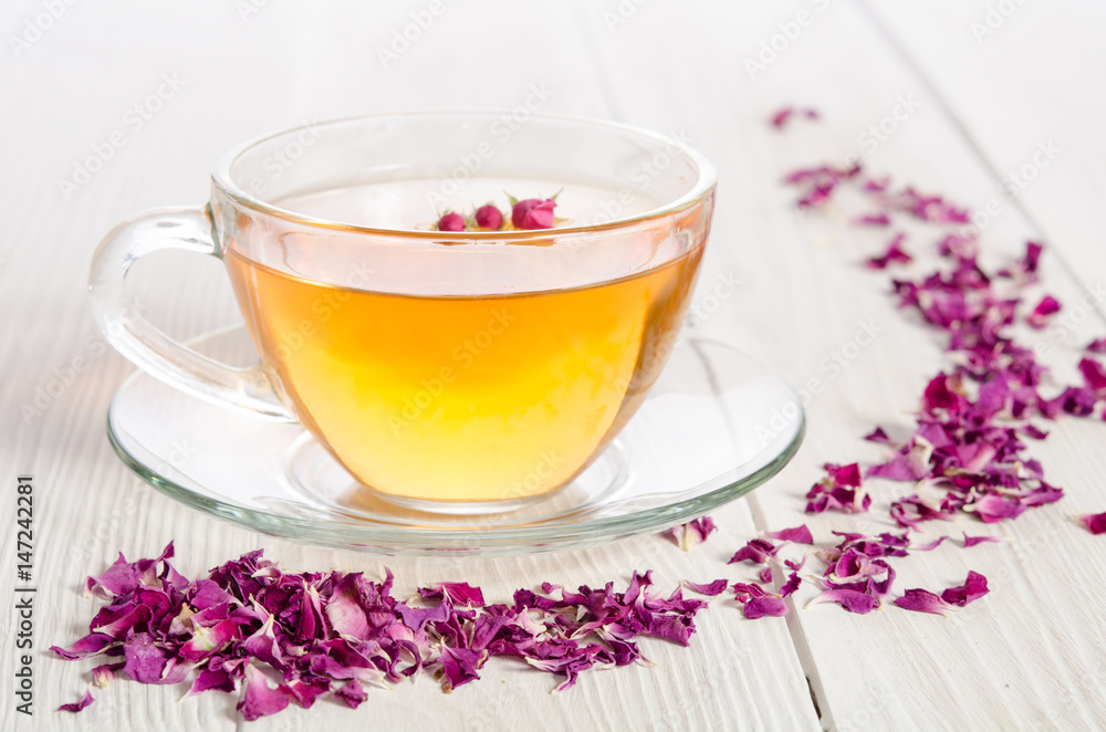 Glass cup of tea with rose petals on the white wooden background Glass cup of tea with rose petals on the white wooden background