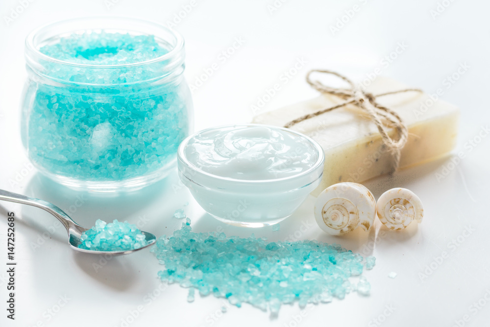 blue bath salt, body cream and shells for spa on white table background blue bath salt, body cream and shells for spa on white table background
