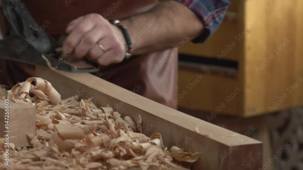 Cabinet Maker Planes Solid Wood in his Workshop/Cabinet maker planes the beech plank with a plane. He works in a small family joiner’s shop. Slow motion Cabinet Maker Planes Solid Wood in his Workshop/Cabinet maker planes the beech plank with a plane. He works in a small family joiner’s shop. Slow motion