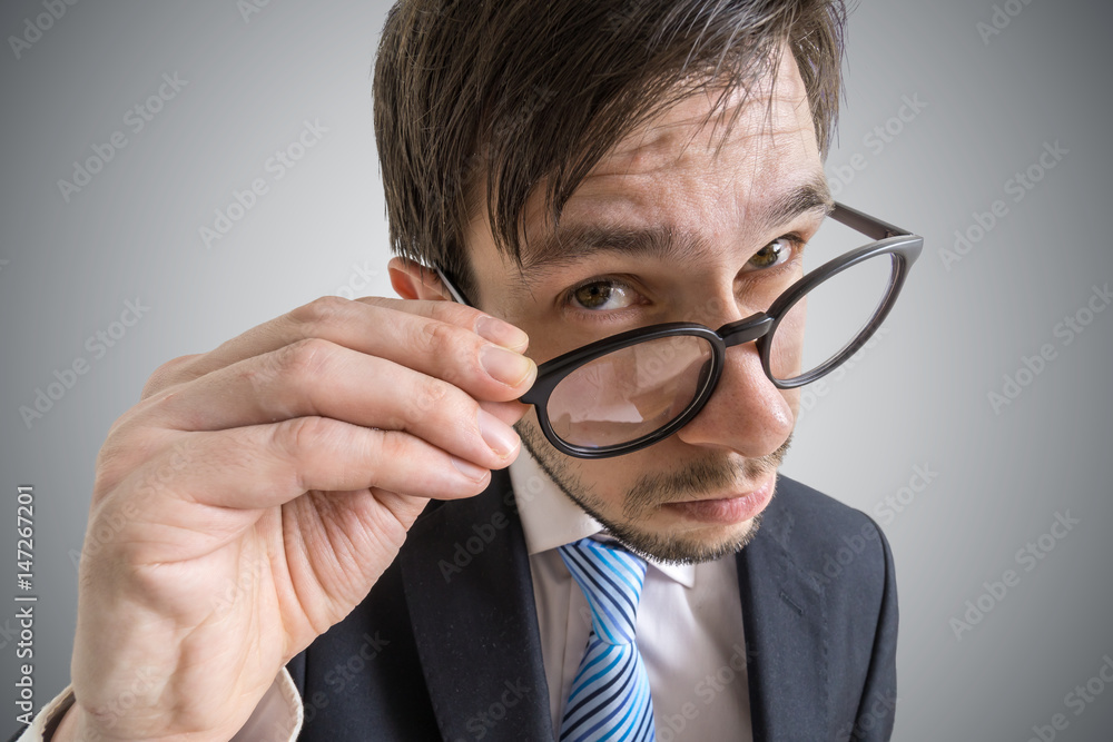 Young suspicious businessman is looking at you through glasses. Young suspicious businessman is looking at you through glasses.