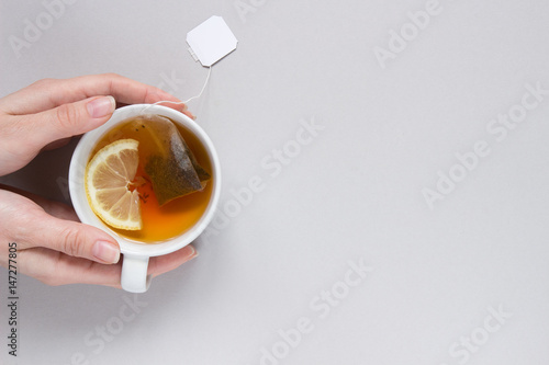 Tea time. Hands holding cup of hot black tea on the blue background, top view