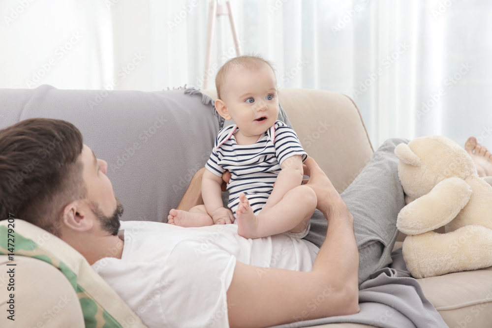 Father lying with cute baby daughter on sofa at home Father lying with cute baby daughter on sofa at home