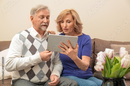 Cute elderly couple with tablet computer at home