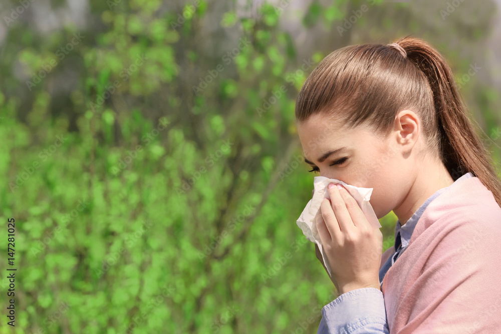 Sneezing young girl with nose wiper among blooming trees in park Sneezing young girl with nose wiper among blooming trees in park