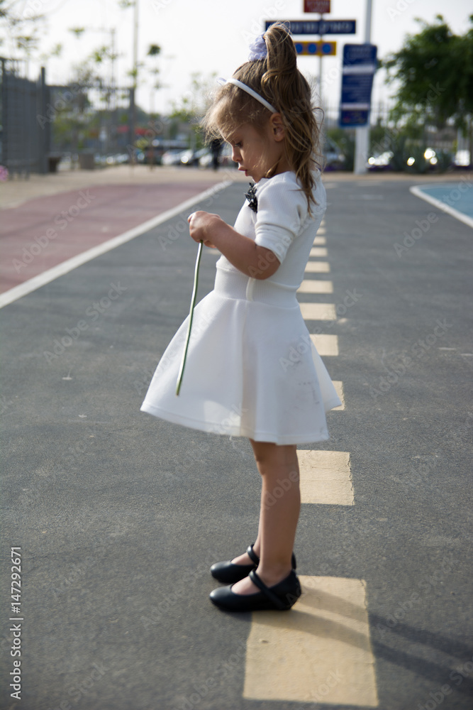 sad little girl in white dress on the road in park sad little girl in white dress on the road in park