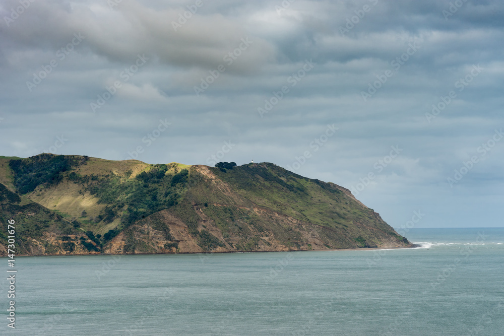 Auckland, New Zealand - March 2, 2017: Manukau Heads at entrance from Tasman Sea into Huia Bay. under heavy cloudscape. Blue-green water. Auckland, New Zealand - March 2, 2017: Manukau Heads at entrance from Tasman Sea into Huia Bay. under heavy cloudscape. Blue-green water.