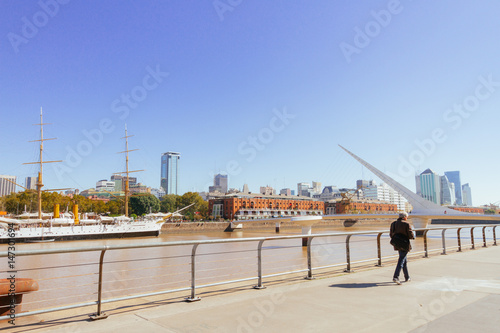 Man walks on a boardwalk in Puerto Madero with background frigate and Women's Bridge