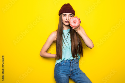 beautiful excited hipster girl in red hat holding pink donut near yellow wall